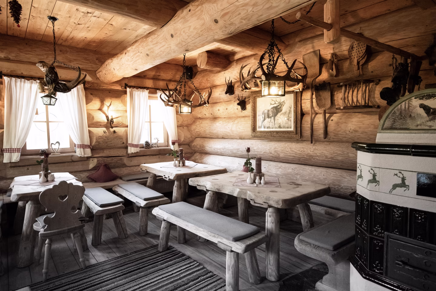 Holzstube mit Hirschgeweihen, Holztischen und traditionellem Kachelofen lädt zur Einkehr ein.