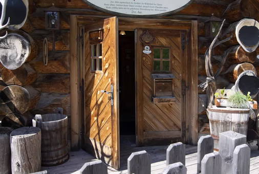 Rustikale Almhütte mit offener Holztür, Geweihen und Fensterläden im Sonnenlicht.