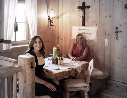 Zwei lächelnde Frauen vom Aar Wirt Team sitzen in urgemütlicher, holzvertäfelter Gaststube an einem rustikalen Tisch.